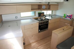 A compact kitchen with a stove, oven, and sink. There is a window above the sink, and a small bench to the right. - Dubrovnik Delight: A Sun-Kissed Sailing Experience (Komolac)