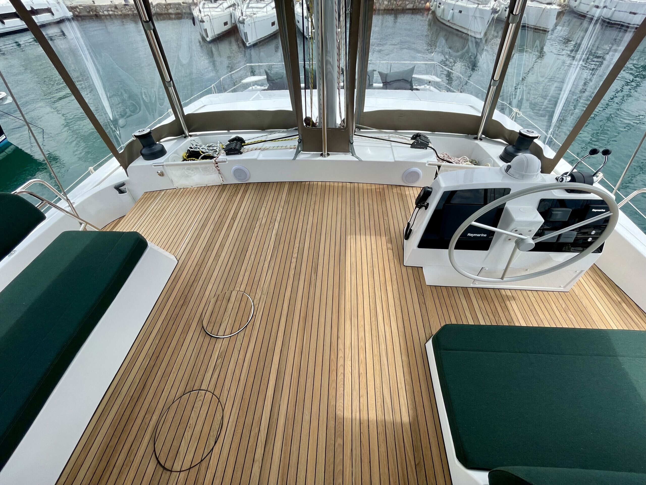 A boat deck with a wooden floor, green cushioned seating, and a steering wheel.