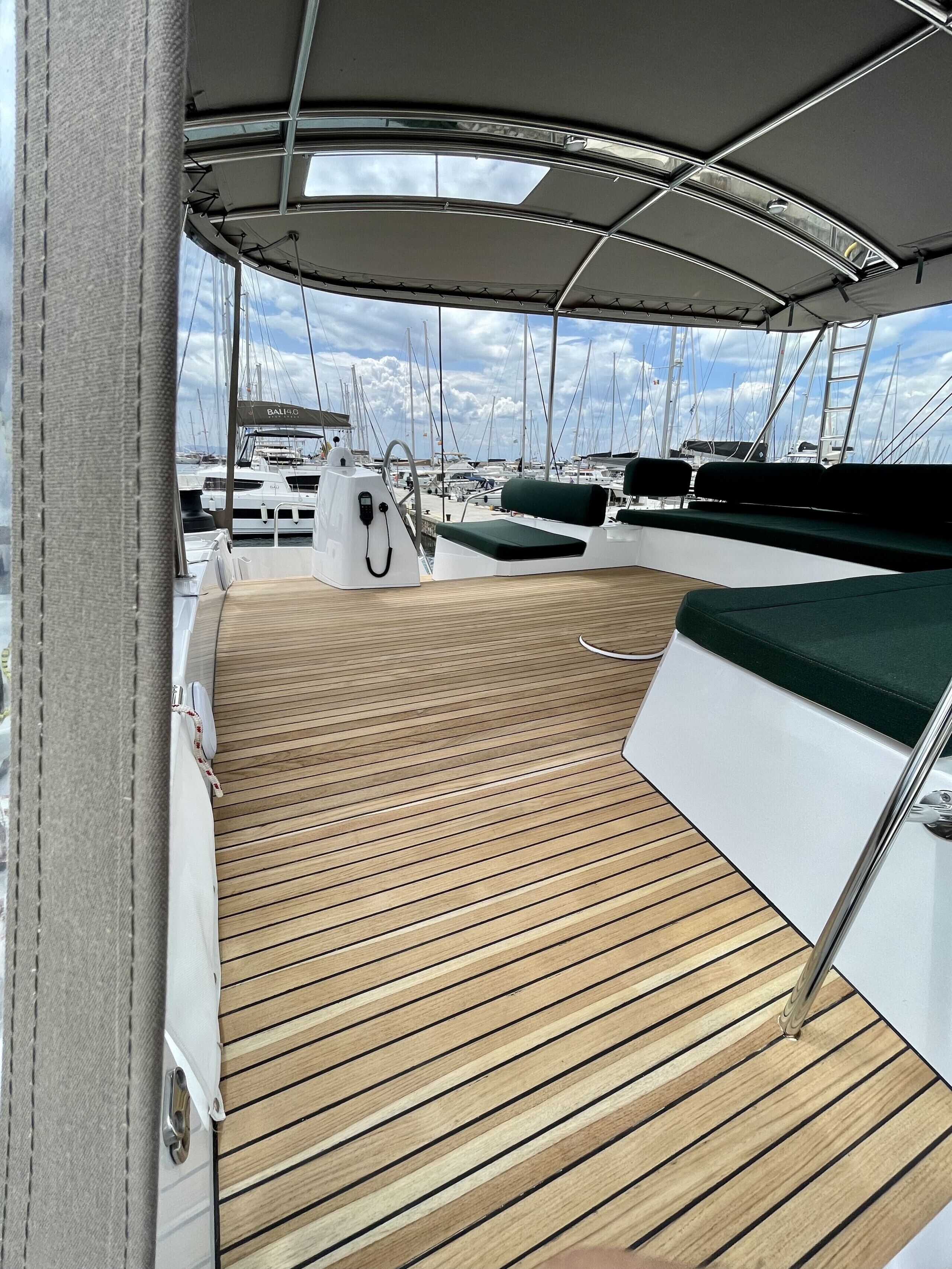 A boat deck with a wooden floor, a white railing, and a view of other boats in the marina.