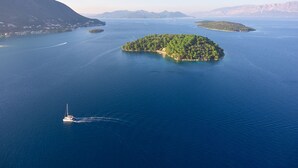 An aerial view of a large island with a small boat in the water. - Sun-soaked Sailing Adventure in the Ionian Islands (Perigiali)