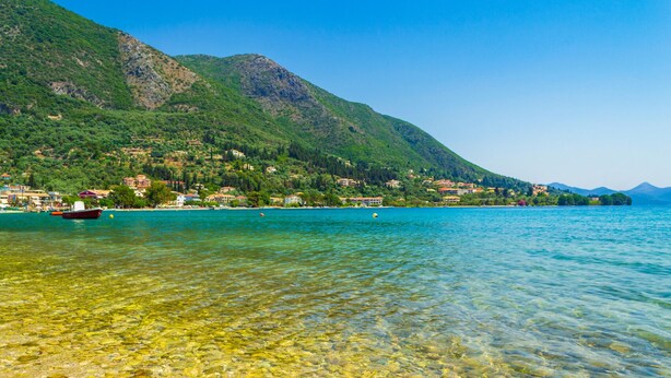 A clear lake with a boat, a mountain, and buildings along the shore. - Sun-soaked Sailing Adventure in the Ionian Islands (Perigiali)