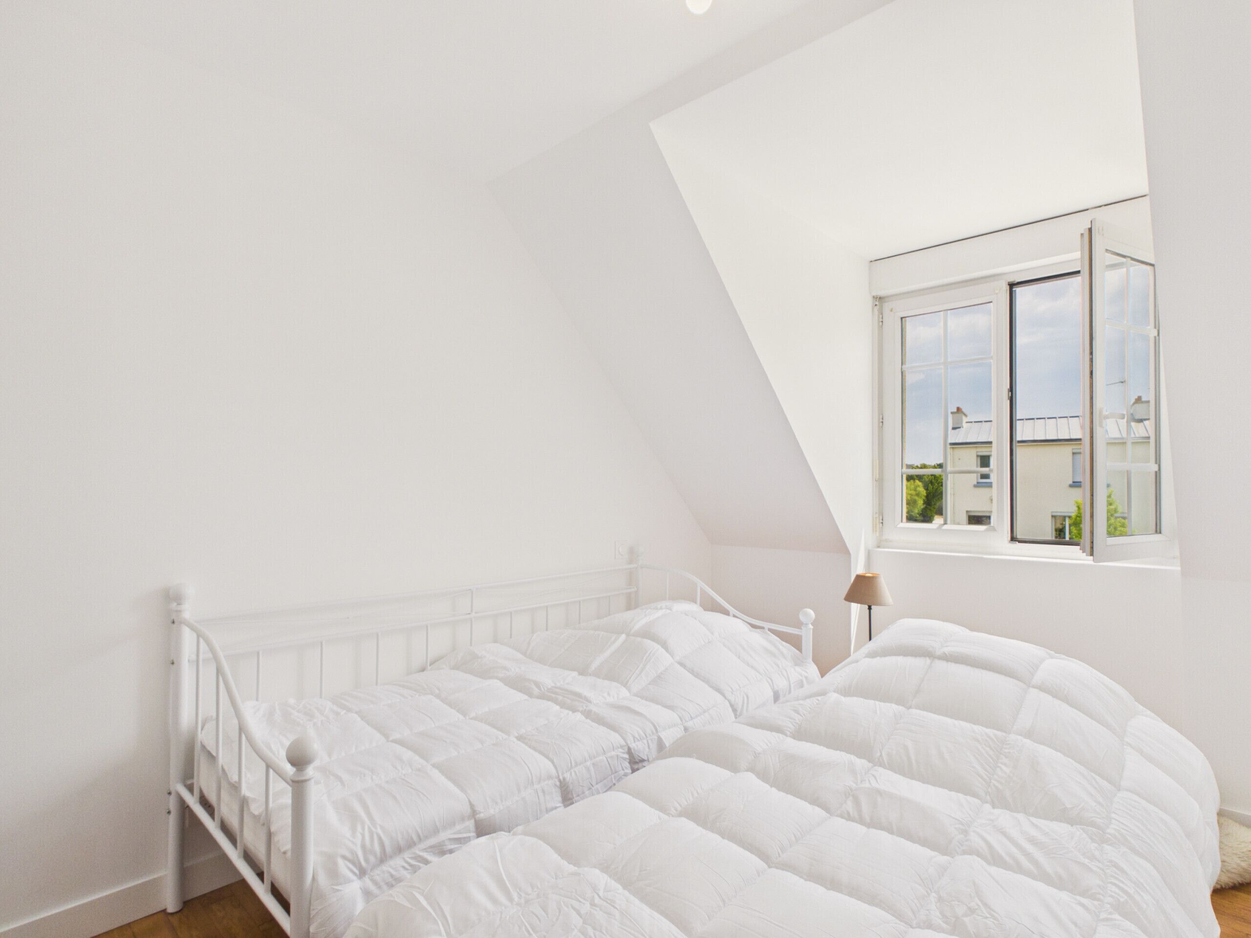Une chambre à coucher avec un lit blanc, une fenêtre et une lampe.