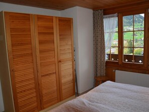 A bedroom with a wooden wardrobe, a window with a view of a green landscape, and a radiator. - Hornflue (Wohlwender) Appartement/Fewo, Dusche oder Bad, WC 2-Bettwohnung by Interhome (Gstaad)