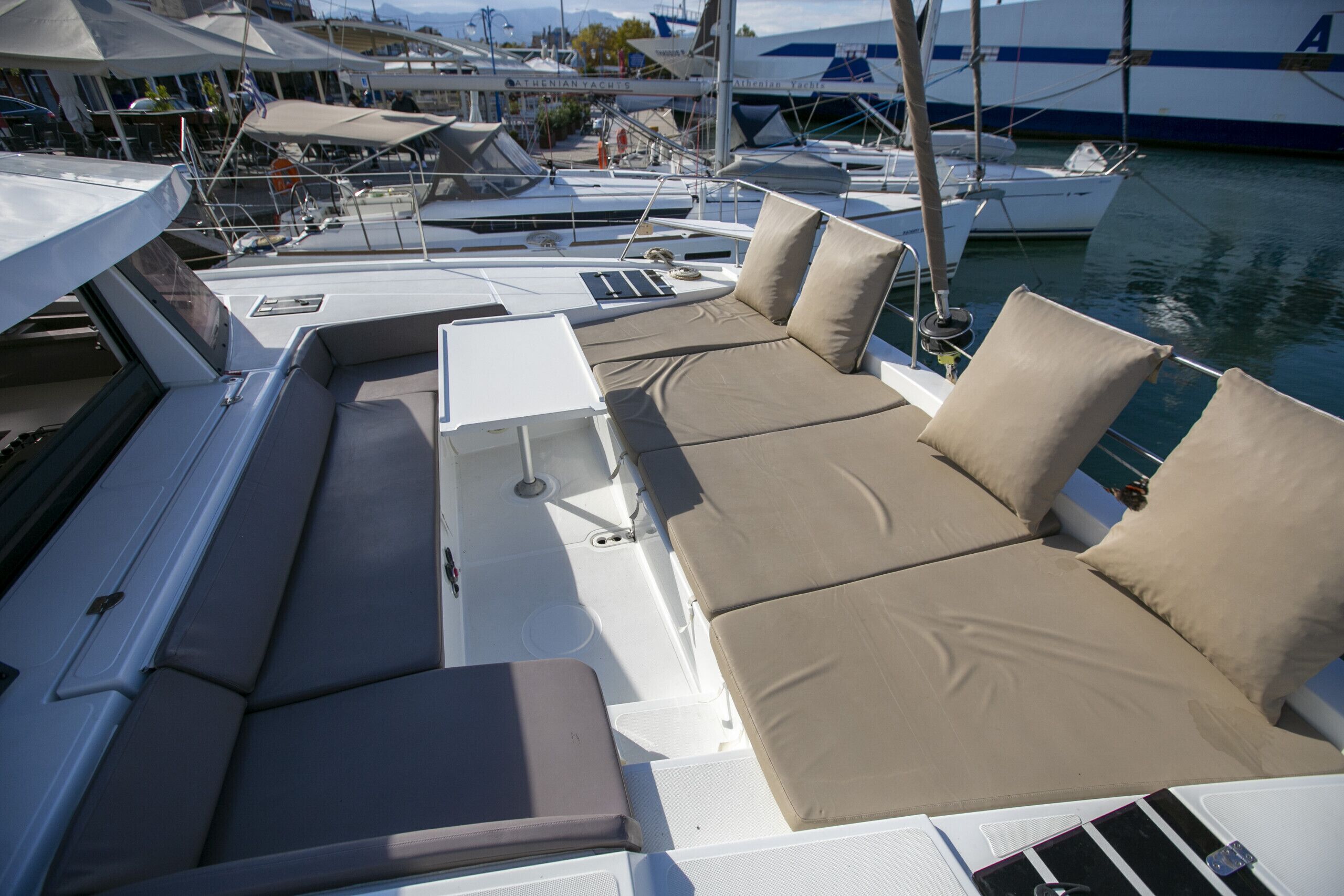 A boat with a sun lounge area, a small table, and a view of other boats in the marina.