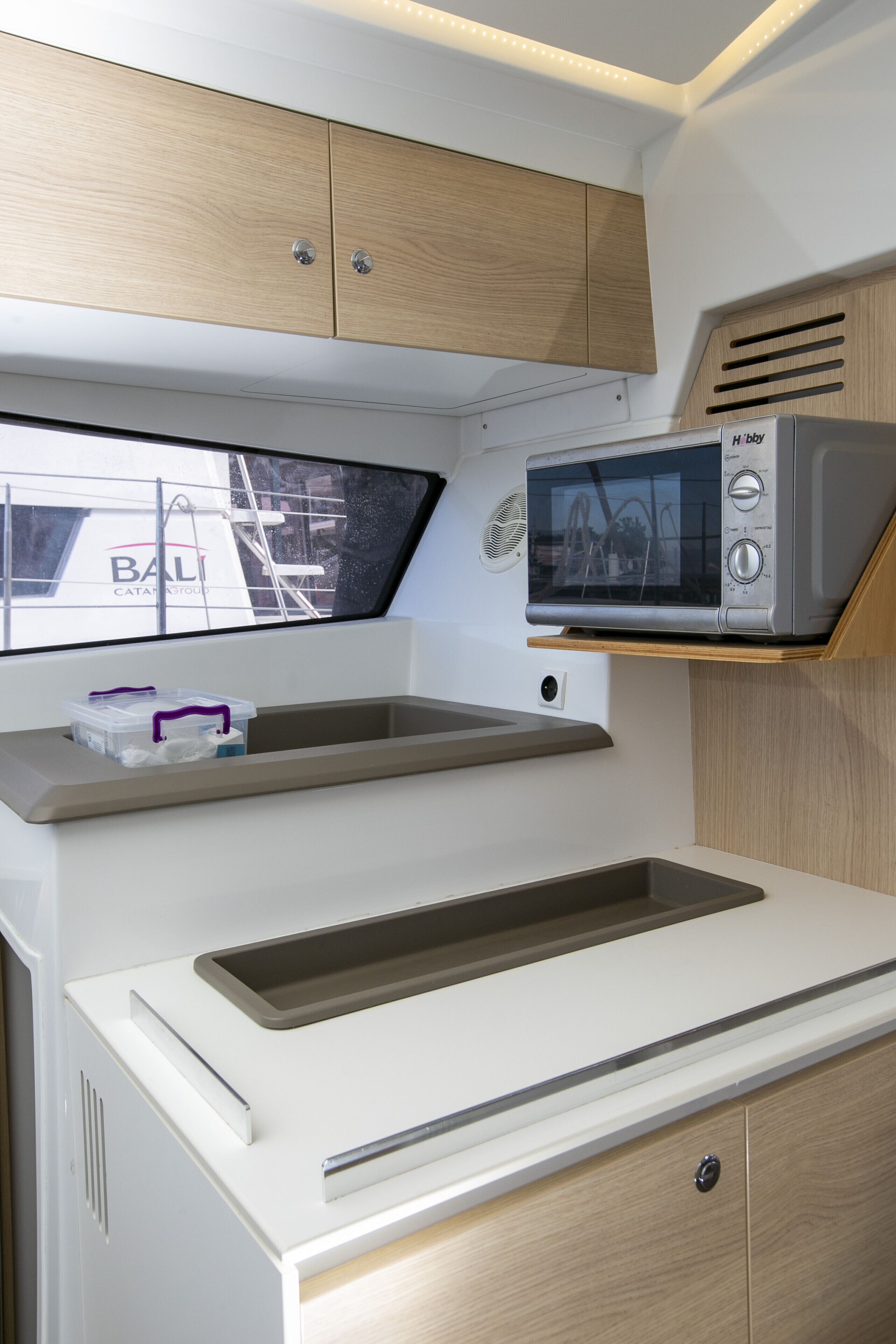 A compact kitchen with a microwave, a window with a view of a building, and a small storage area.