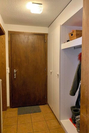 Ein Flur mit Holztür, einem weißen Schrank mit Regalen und einem gefliesten Boden.
