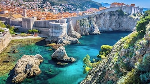 Eine Küstenstadt mit einer historischen Steinbrücke, klarem türkisblauem Wasser und einem bergigem Hintergrund.