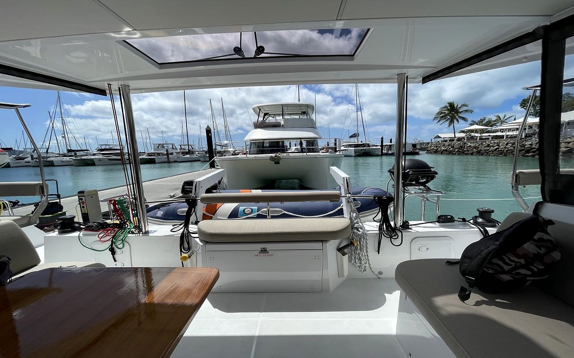 A boat deck with a seating area, a wet locker, and a view of the marina with other boats and a building in the background.