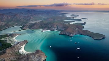 Eine Luftaufnahme einer Küstenregion mit klarem türkisblauem Wasser, felsigem Gelände und mehreren Booten.