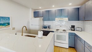 Une cuisine moderne avec des plans de travail blancs, des armoires bleues, une cuisinière blanche, un four à micro-ondes et un grille-pain.
