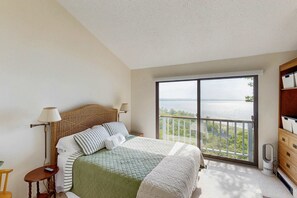 Ein Schlafzimmer mit Bett, Nachttisch, Lampe, Kommode und einem Balkon mit Blick auf das Wasser.