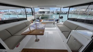 A boat interior with a table, cushioned seating, and a view of the marina. - Sun-Kissed Sailing Adventure in Gran Barrera de Coral from Playa Airlie, Queensland (Airlie Beach)