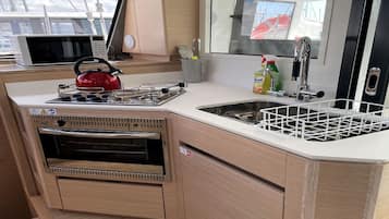 A compact kitchen with a microwave, kettle, sink, and storage cabinets.
