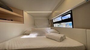 A bed with white linens, a window with a view of the sea, and a shelf with a wooden object. - Sun-Kissed Sailing Adventure in Gran Barrera de Coral from Playa Airlie, Queensland (Airlie Beach)