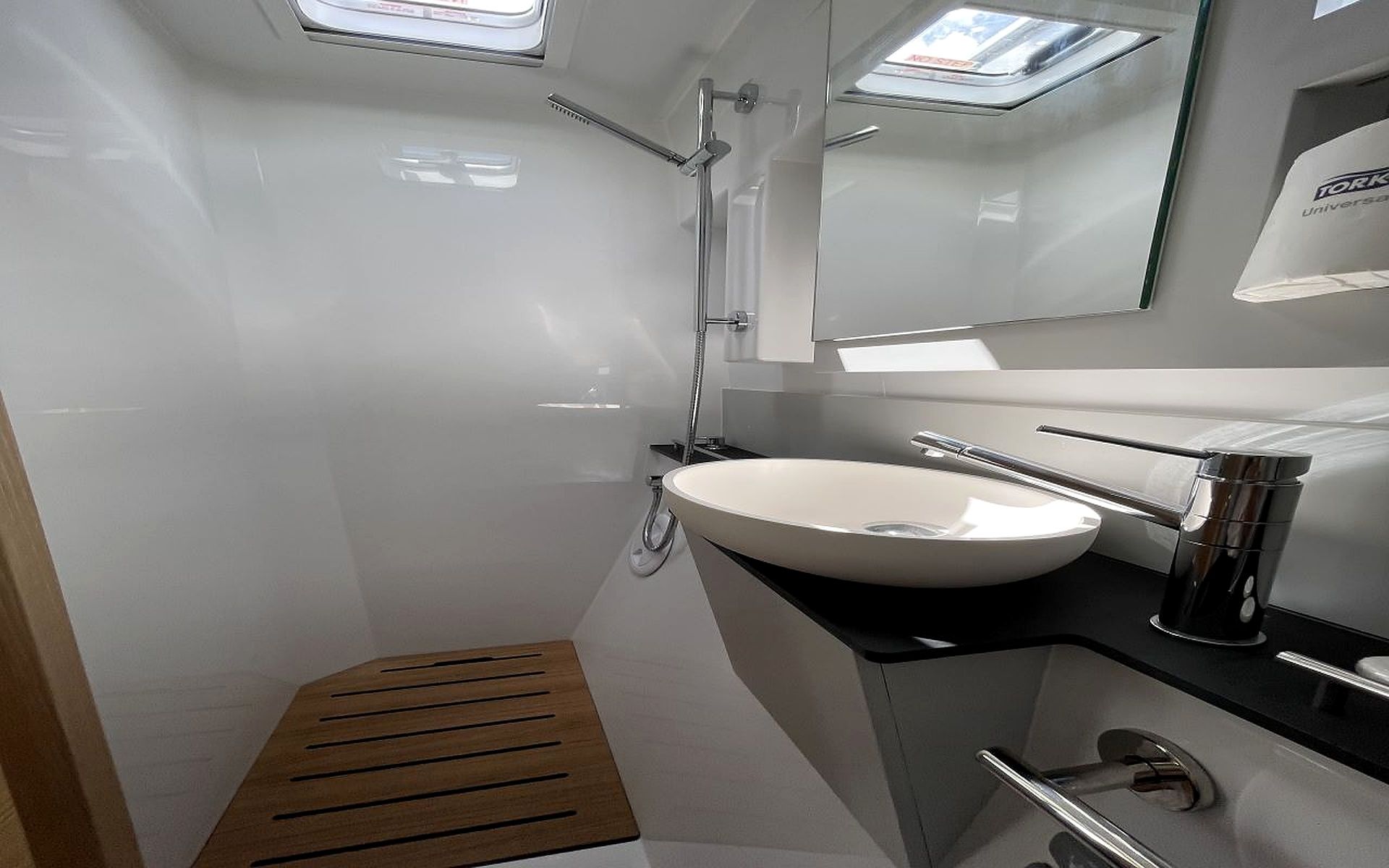 A modern bathroom with a white sink, a shower, and a skylight.