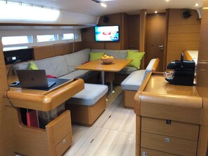 A compact, well-lit interior with a seating area, a table with a bowl of fruit, a coffee machine, and a television mounted on the wall. - Sun-Kissed Sailing Adventure in the Ionian Islands, Lefkada (Lefkada)