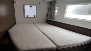 Ein kleiner Wohnmobilvan mit einem Einzelbett, dessen Matratze ein gewelltes Muster aufweist, einem Fenster mit Vorhängen und einer Wandleuchte.