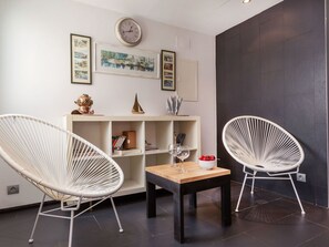 A modern living room with two white wicker chairs, a wooden coffee table, and a bookshelf with decorative items. - Punta Aromir by Interhome (Tossa de Mar)