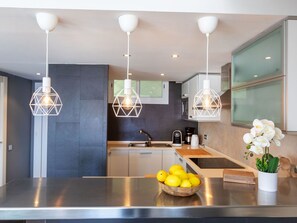 A modern kitchen with stainless steel countertops, a bowl of lemons, and pendant lights. - Punta Aromir by Interhome (Tossa de Mar)
