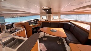A compact galley with a sink, stove, and microwave, a small table, and a seating area with cushions. - Sun-Kissed Sailing Adventure in Gran Barrera de Coral from Playa Airlie, Queensland (Airlie Beach)