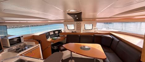 A compact galley with a sink, stove, and microwave, a small table, and a seating area with cushions.