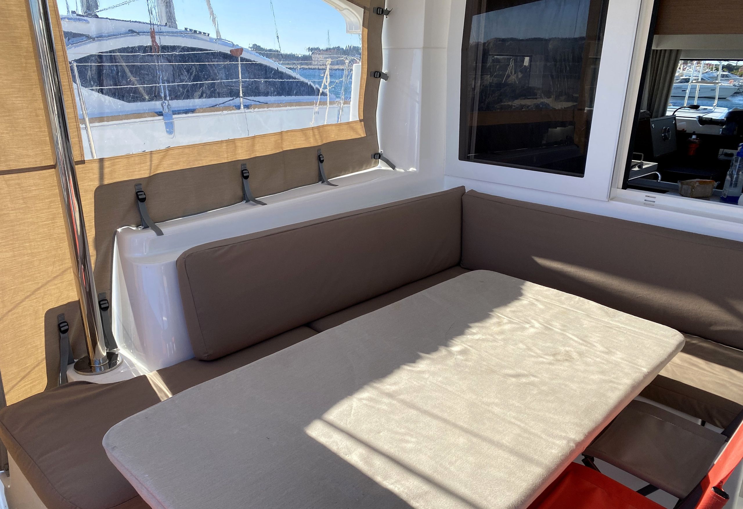 A cabin interior with a bench seat, a window with a view of boats, and a small table.