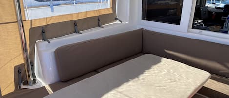 A cabin interior with a bench seat, a window with a view of boats, and a small table.