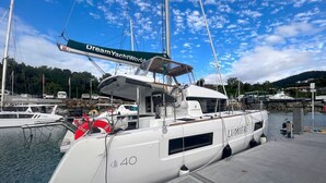 Un yate blanco amarrado en un puerto deportivo, con un letrero que dice 'Dream YachtWorld', el logo 'LUMIERS' y el número '40' en su costado.