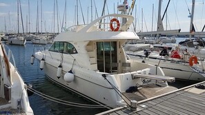 A white yacht docked at a marina with multiple boats, a lifebuoy, and a clear sky.