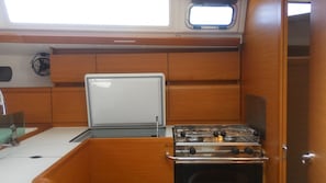 A compact galley with a stove, a small window, and wooden cabinetry. - Sun-Kissed Sailing Adventure in Islas Sarónicas (Alimos)