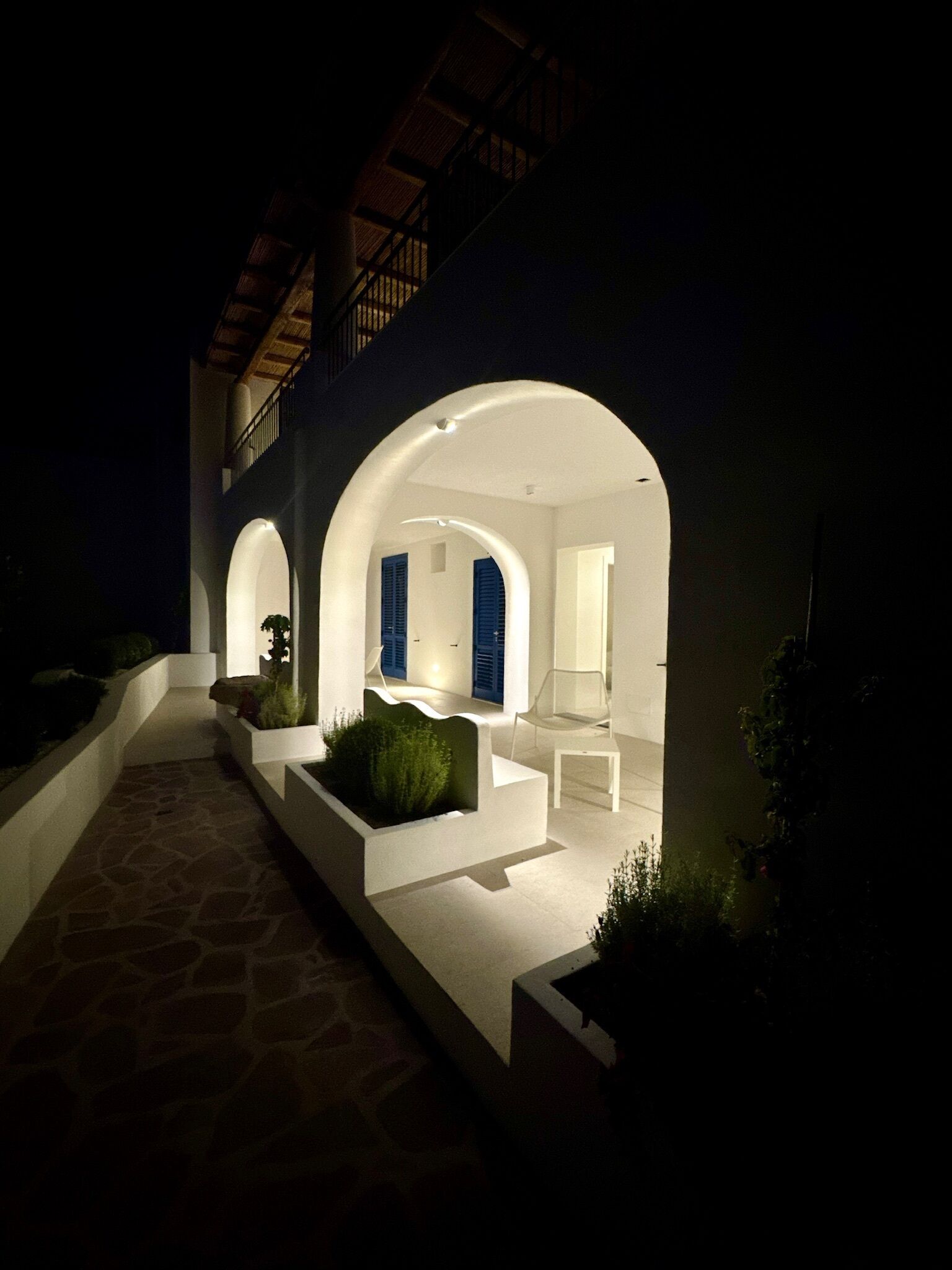 A modern outdoor patio area with white walls and arches, stone flooring, and minimalistic furniture.
