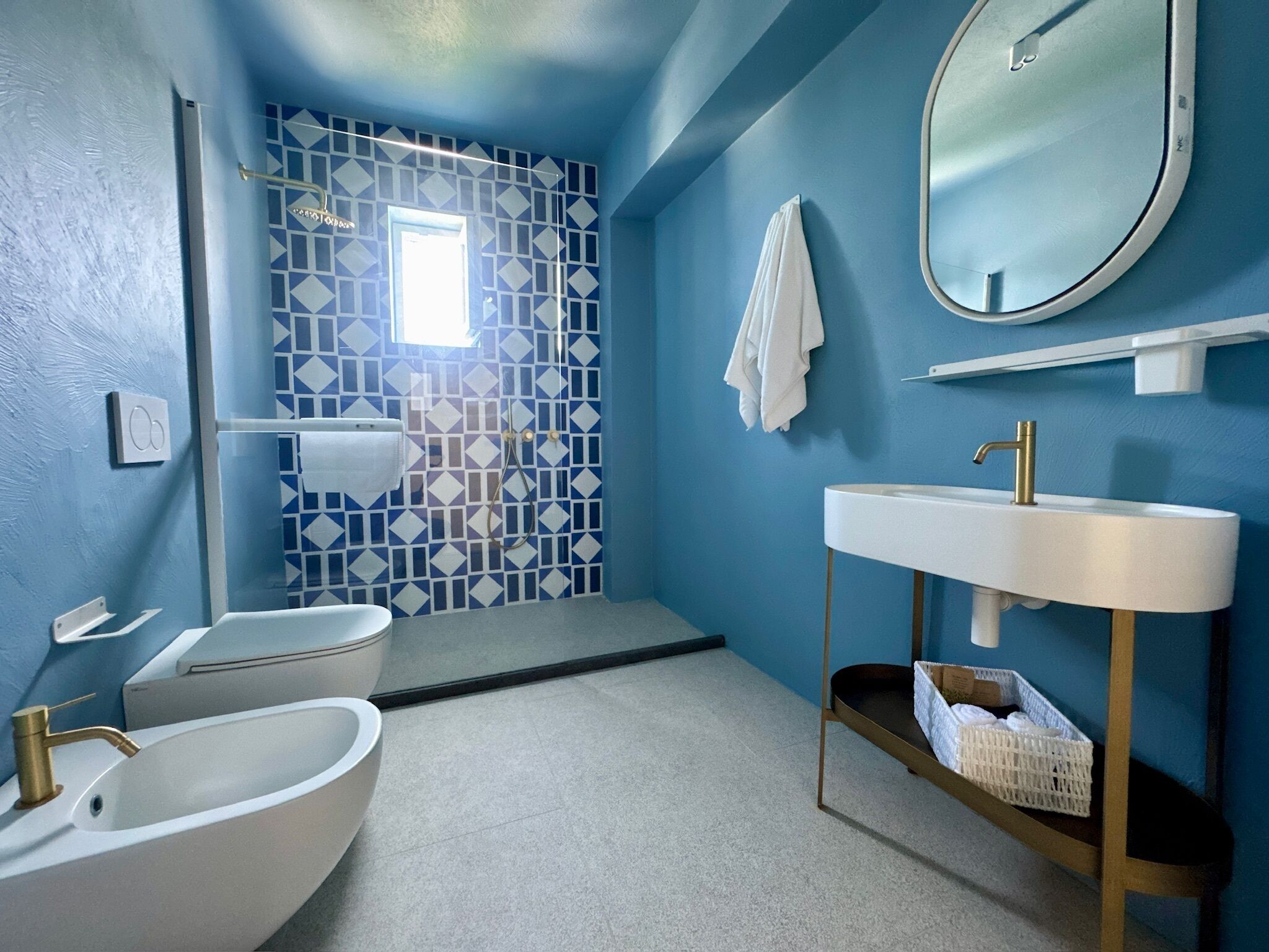 Une salle de bain avec une baignoire, un lavabo avec un robinet doré, une douche avec un mur recouvert de carreaux aux motifs géométriques et un miroir sur le mur.