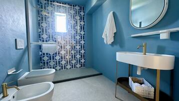 Une salle de bain avec une baignoire, un lavabo avec un robinet doré, une douche avec un mur recouvert de carreaux aux motifs géométriques et un miroir sur le mur.