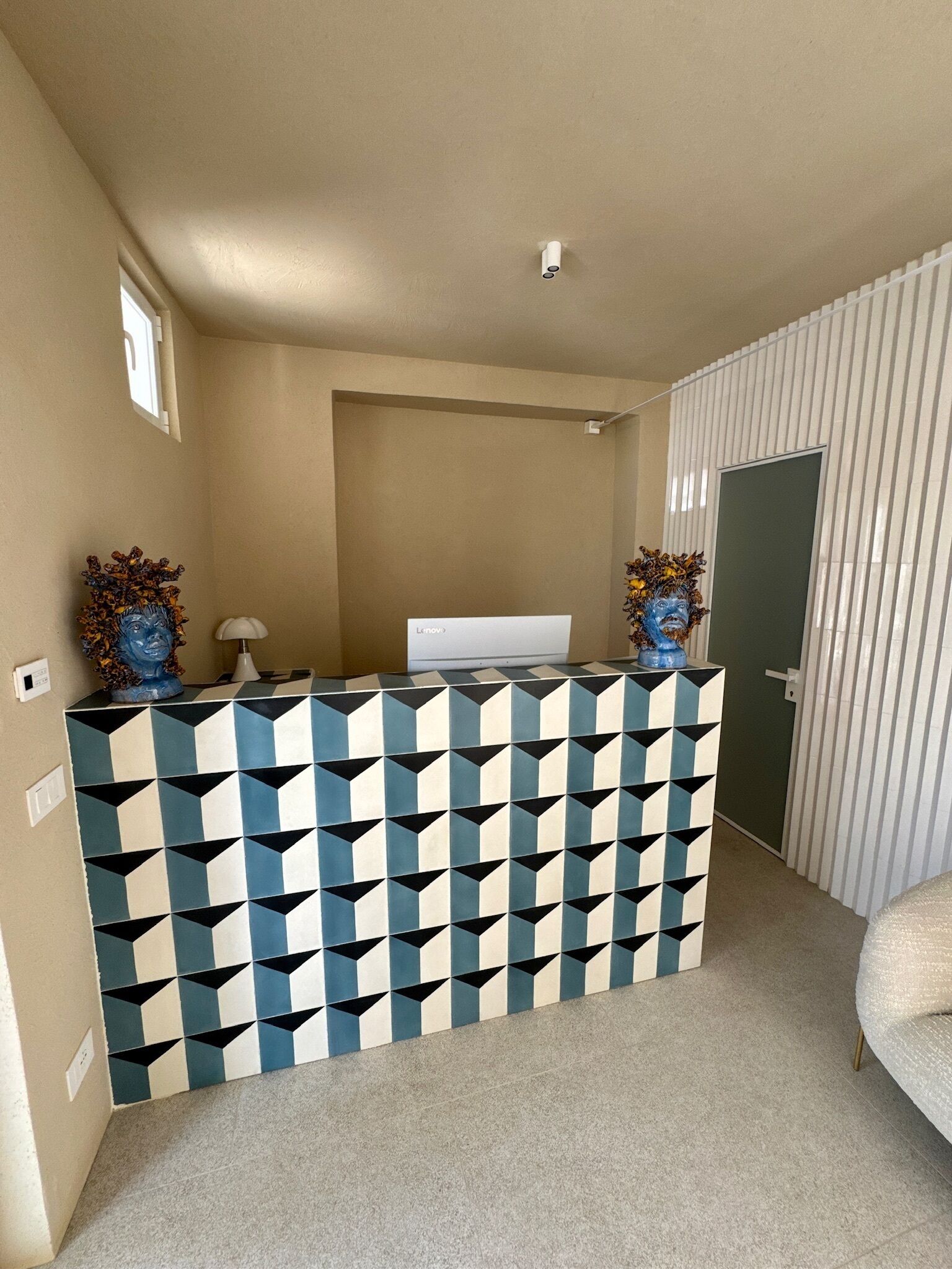 A reception desk with a geometric tile pattern, a white wall-mounted TV, and a door with vertical blinds.