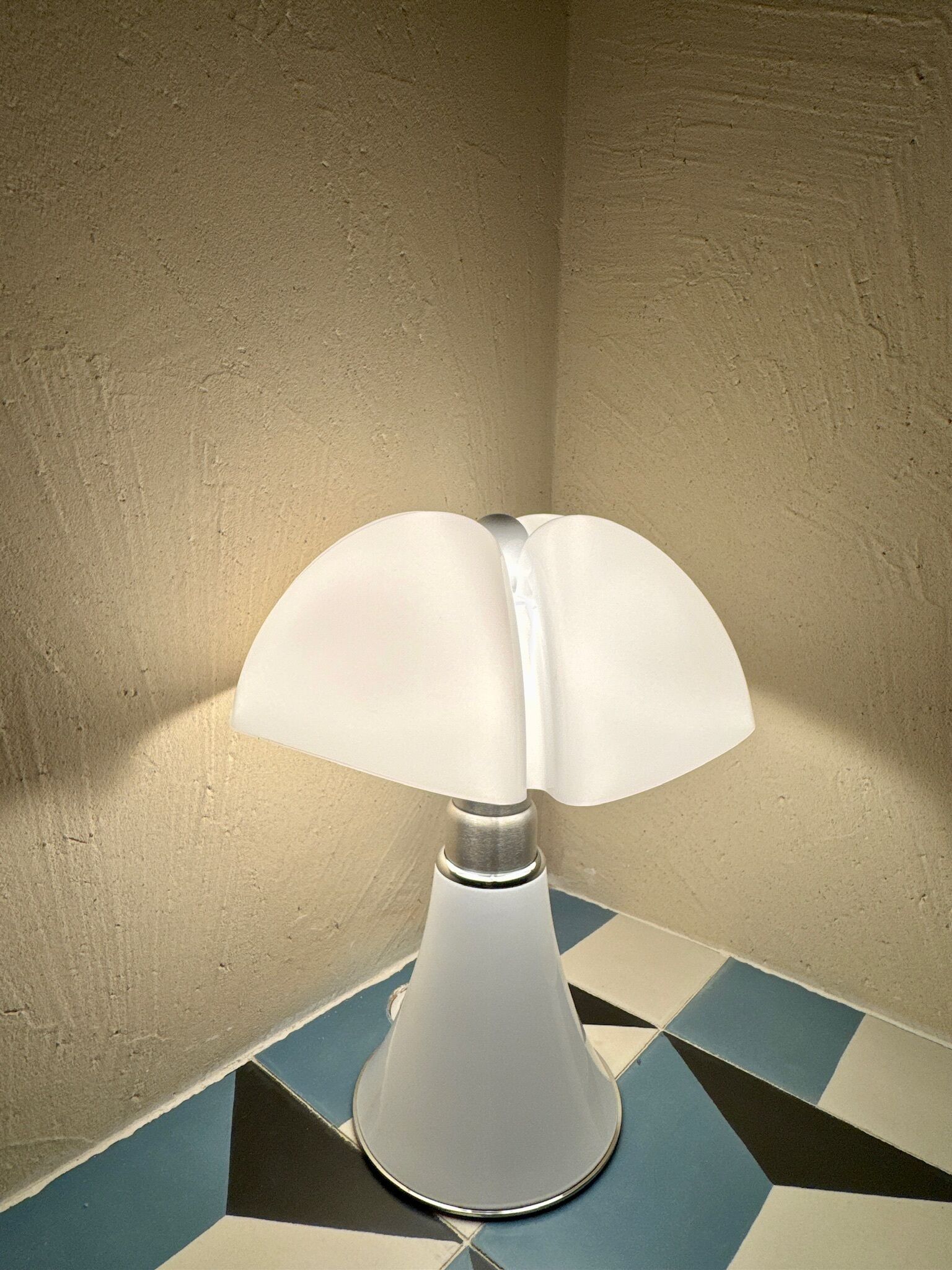 A corner lamp with a white shade on a tiled floor.
