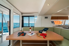 A cabin with a table, a bottle, a box, and a view of the sea. - Sun-Kissed Sailing Adventure in the Ionian Islands (Nikiana)