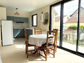 A modern kitchen with a dining table and chairs, a refrigerator, and a large window with a view of houses. - Qhome 7 - Bright 2-room apartment between Paris and Disney (Noisy-le-Grand)