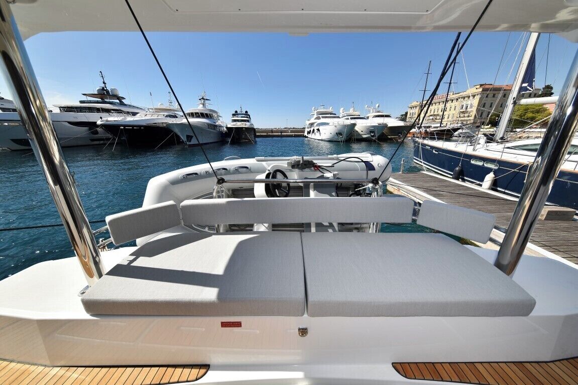 Een dek van een boot met zitplaatsen, een stuurwiel en een uitzicht op andere boten in een jachthaven.