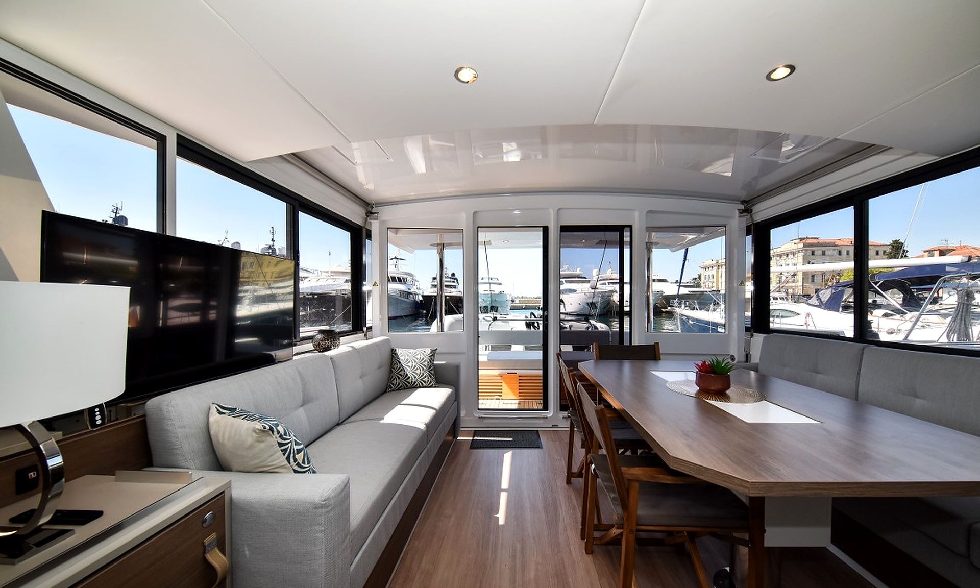 A modern interior with a sofa, dining table, and large windows overlooking a marina.