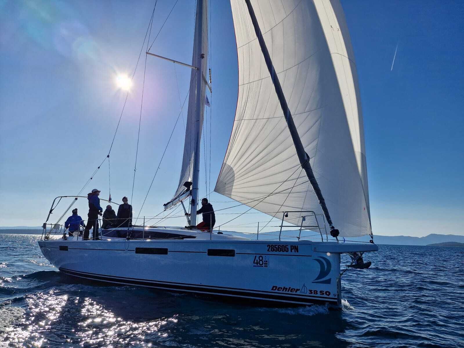 Eine Segelyacht mit Personen an Deck, bewölkter Himmel und ruhige See.