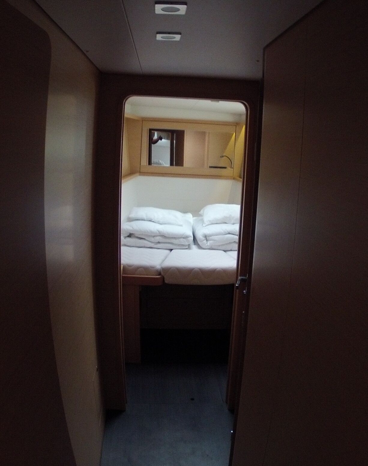 A narrow corridor leading to a small bedroom with a bed, a mirror, and a window.