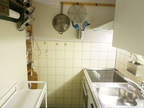 A kitchen with white tiles, stainless steel sinks, a hanging pot rack, and various kitchen utensils. - La Sarine 13 Studio, Dusche oder Bad, WC 2-Bettwohnung by Interhome (Gstaad)