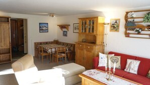 Ein Wohnzimmer mit einer Couch, einem Esstisch mit Stühlen, einer Holzkommode und einem roten Sitzsofa.