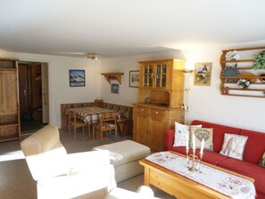 Ein Wohnzimmer mit einer Couch, einem Esstisch mit Stühlen, einer Holzkommode und einem roten Sitzsofa.