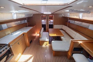 A boat interior with a dining area, seating, and a galley with a stove. - Sun-kissed Sailing Adventure in Split-Dalmatia, Croatia (Seget Donji)