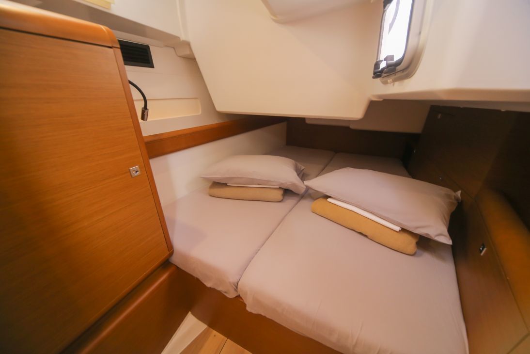 Une cabine compacte et bien éclairée, équipée d’un lit simple, d’un petit placard de rangement et d’une fenêtre.