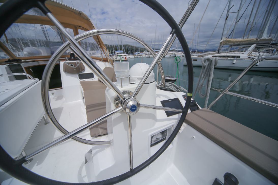 A boat's steering wheel, part of the deck, and a view of other boats in the marina.