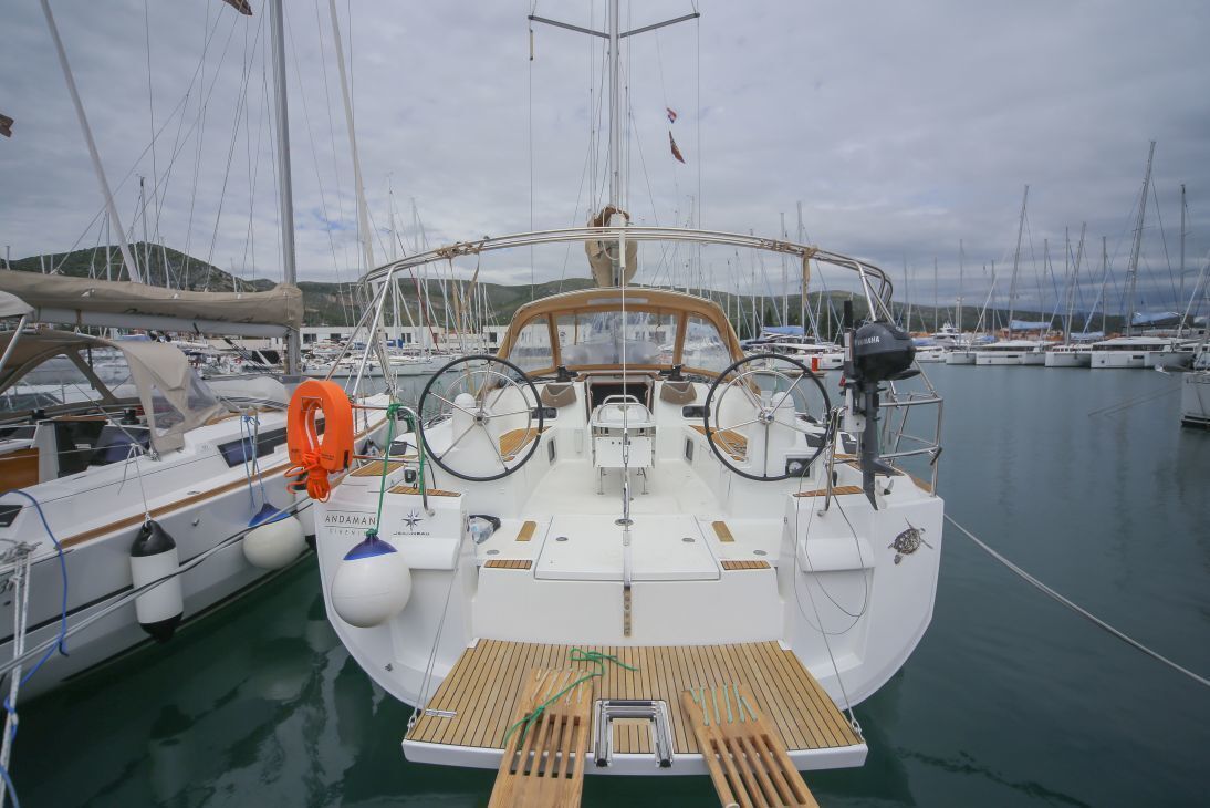 Eine Yacht liegt in einer Marina festgemacht, mit mehreren Booten, einem Steuerrad und einem Rettungsring.