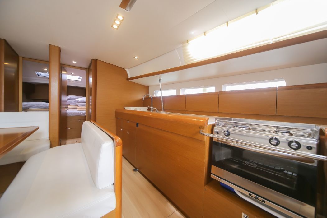 A compact kitchen with a built-in oven, a dining area with a bench, and a small sleeping area with a bed.