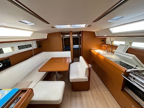 A compact interior with a central table, seating, a kitchenette, and overhead lighting. - Sun-Kissed Sailing Adventure in Zadar, Croatia (Bibinje)